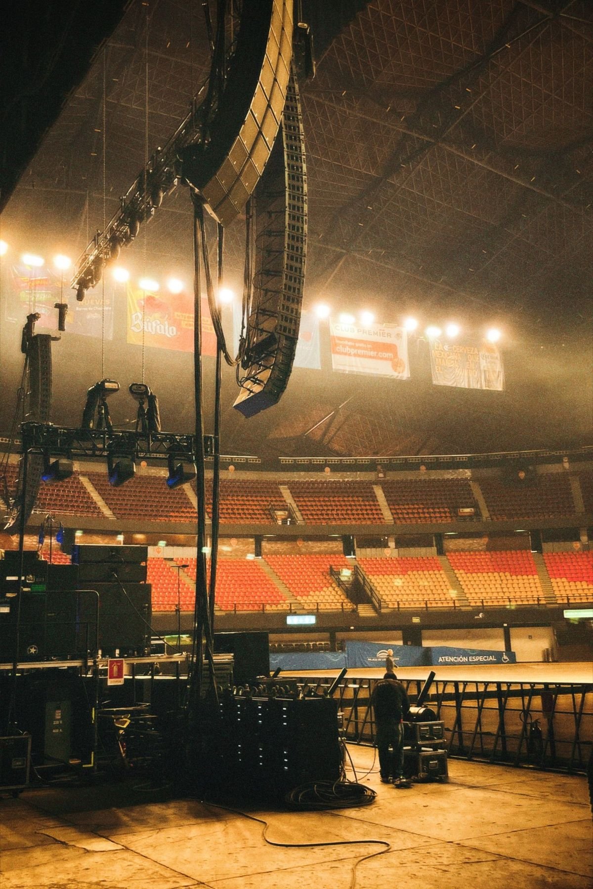 Arena floor with a flown line-array PA and lighting truss before doors