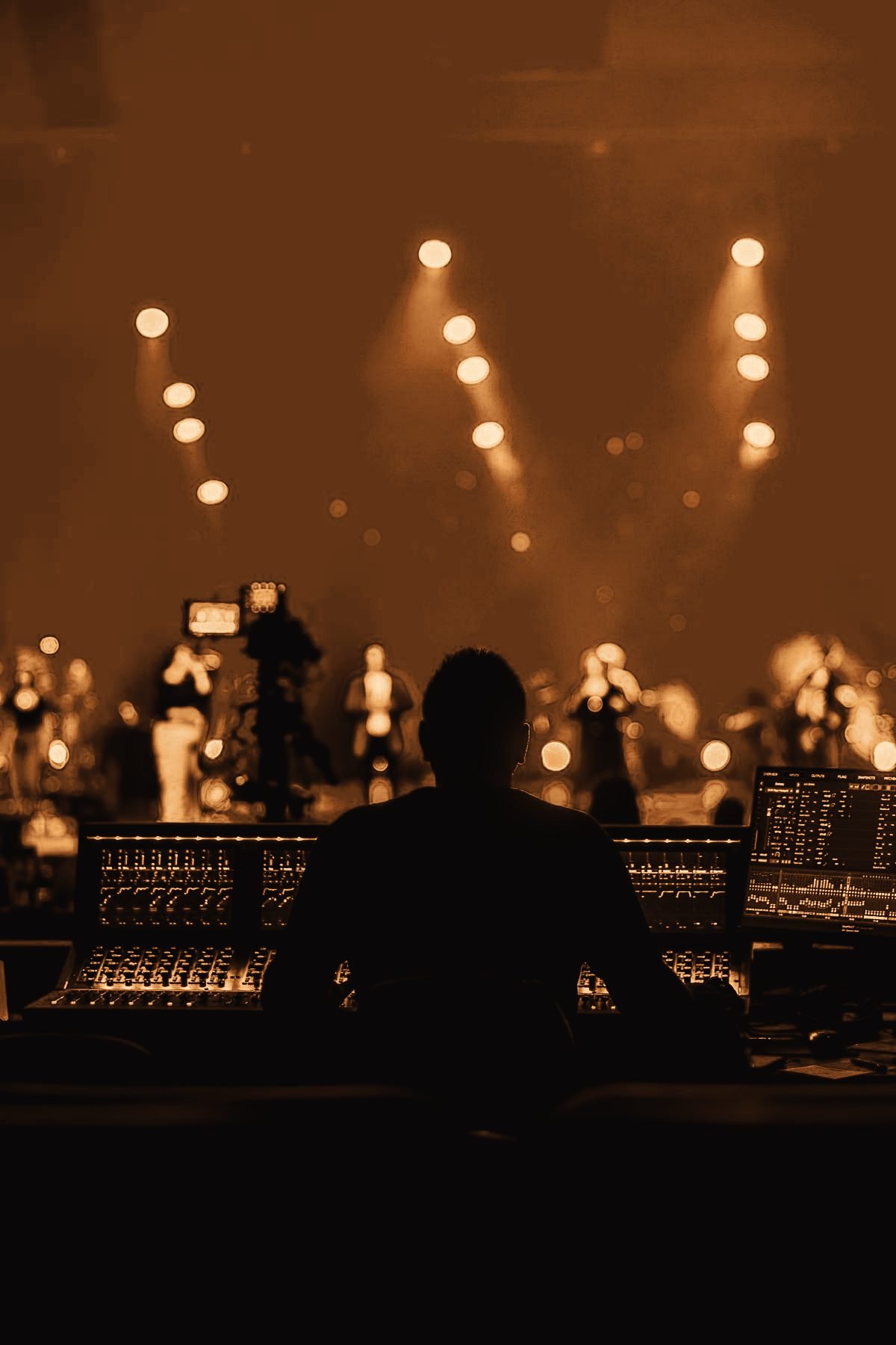 Front-of-house engineer at a digital mixing console facing a lit stage
